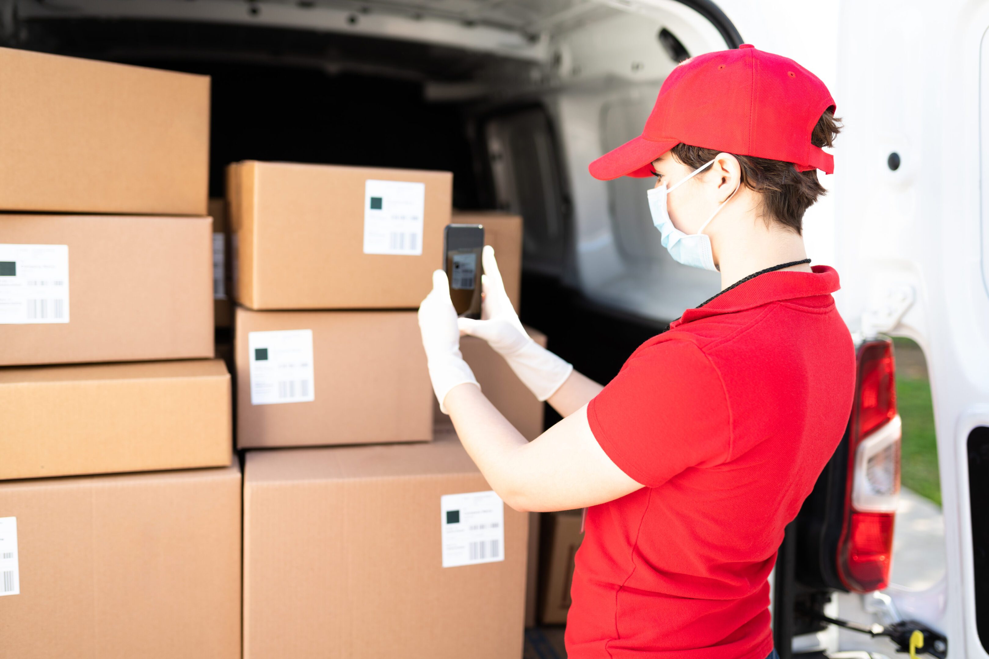 Rear view of a caucasian female worker scanning the barcode of a shipping label in a package. Delivery woman using a smartphone while delivering a parcel