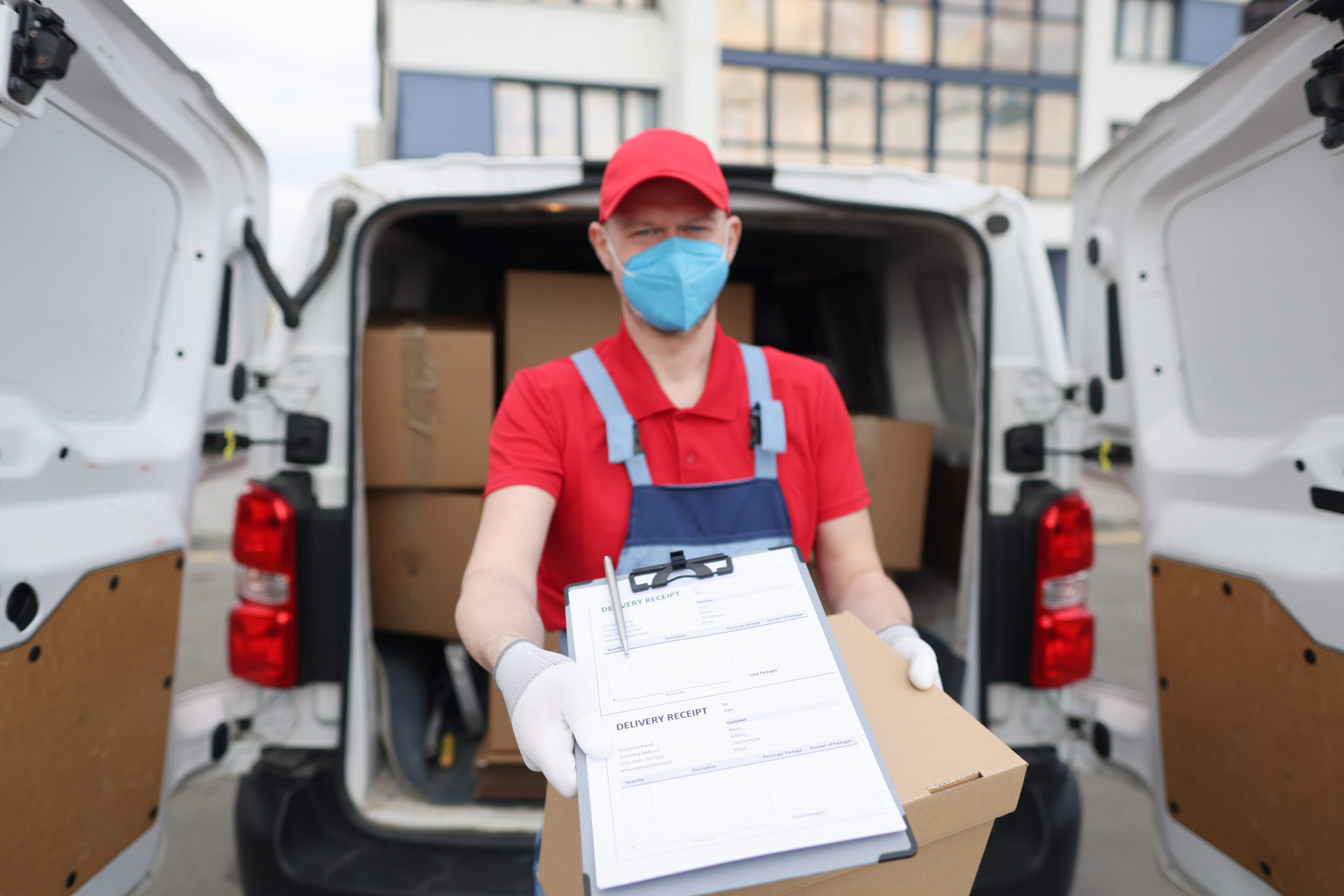 Courier driver in medical protective mask and gloves holds out documents with delivery receipt. Safe customer service for cargo delivery concept